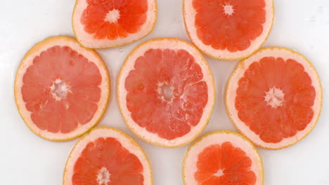 top view: on a white background a many fresh grapefruit is lying in the water water drops are falling from above and splashes are falling in slow motion in all directions.