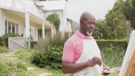 Senior-african-american-man-painting-on-wooden-easel-in-garden,-slow-motion