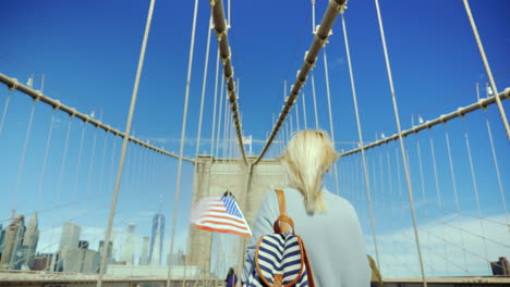 a tourist with a flag of america and a backpacker is walking along the famous brooklyn bridge in new