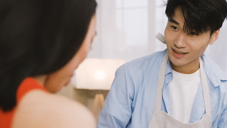 Vista-De-Cerca-De-Un-Hombre-Japonés-Usando-Un-Delantal-Mientras-Cocina-Y-Habla-Con-Un-Amigo-En-La-Cocina