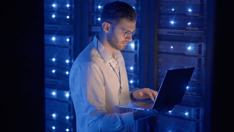 data center it specialists coworking in secure server room of cyberspace. male administrator pointing at error server cabinet running diagnostics on laptop computer