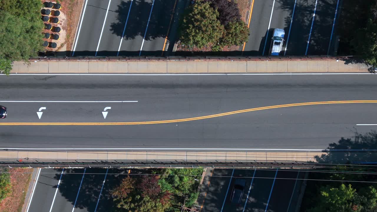 An aerial, top down view of an overpass crossing the Southern State Parkway on Long Island, NY in the morning. Some traffic travels in all directions as the camera is tilted down and is stationary
