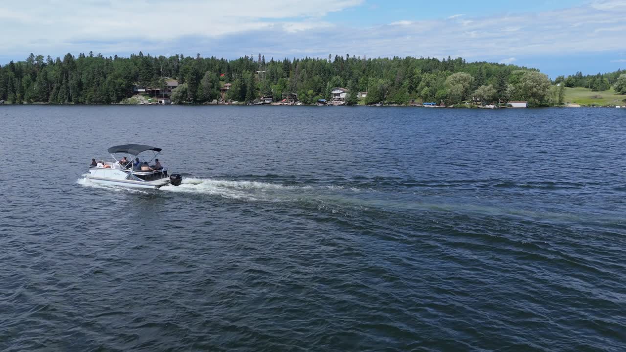 Aerial drone shot of a motorboat cruising across a calm blue lake with forest shoreline in the background