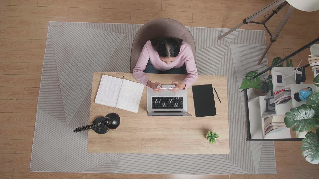 집에서 나무 책상에 앉아 스마트폰에서 게임을 하는 여자의 상단 시각