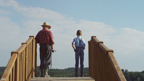 rear view of a teen boy and his grandfather fishing in the wooden bridge