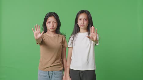 young asian women with bruise bodies looks into camera showing hands sign to stop the violence in the green screen background studio