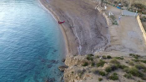 Aerial-drone-shot-captures-a-kayaker-at-Es-Bol-Nou-beach,-preparing-his-kayak-on-the-sandy-shore-against-a-backdrop-of-clear-blue-waters