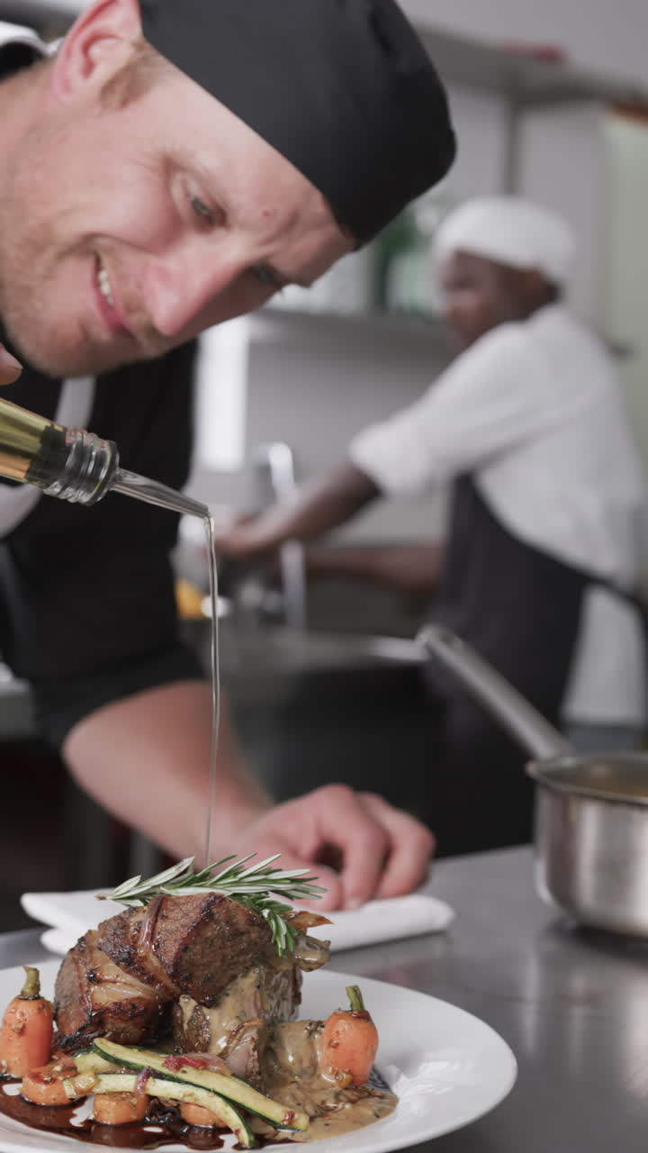 Focused caucasian male chef pouring olive oil on prepared meal in kitchen, slow motion, vertical