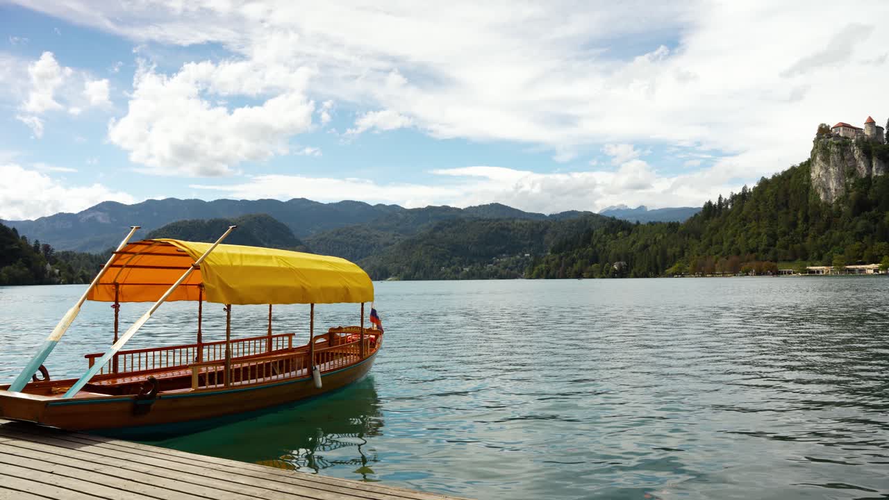 Classica imbarcazione Pletna che galleggia sulle acque tranquille di un lago con montagne sullo sfondo e tenui riflessi: perfetta per viaggi, turismo e splendidi contenuti visivi