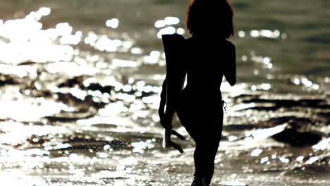 silhouette of woman running out the sea with her surfboard