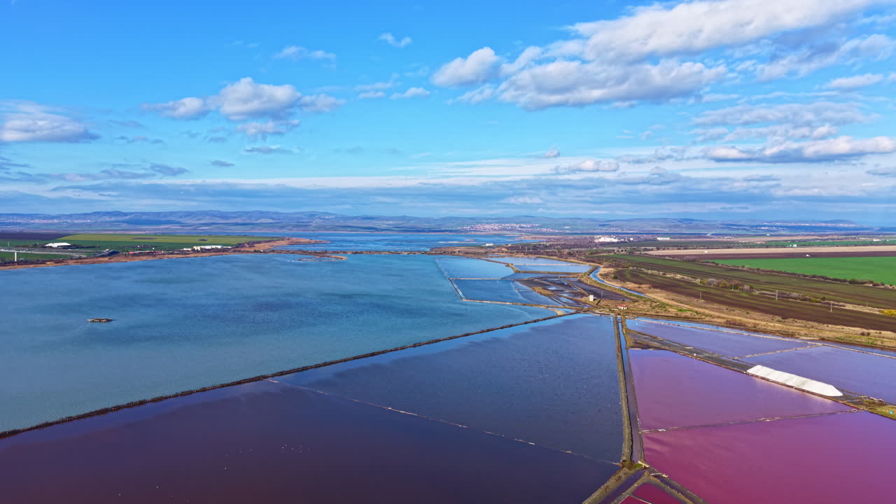 Naturskøn udsigt over levende sletter med salt, der afspejler blå himmel og lette skyer nær en rolig bugt ved middagstid