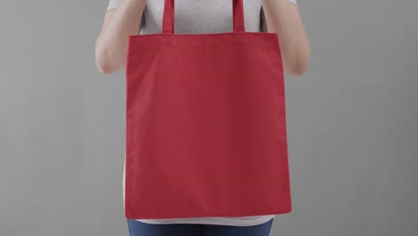 mujer caucásica con camiseta blanca sosteniendo una bolsa roja sobre un fondo gris, espacio de copia, cámara lenta