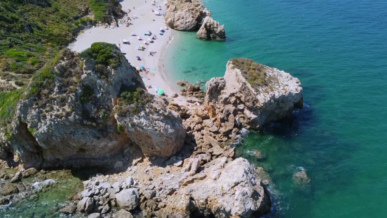 Ripresa cinematografica con drone che sorvola un'enorme formazione rocciosa per rivelare la spiaggia nascosta di Potistika. Veduta dall'alto delle acque turchesi dell'Egeo e della sabbia dorata. Splendido paesaggio costiero. Nessun audio.