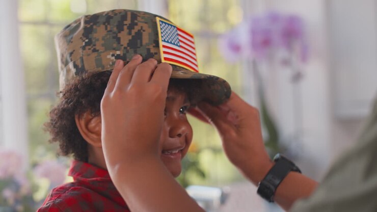Madre soldatessa americana in uniforme a casa in congedo che mette il berretto dell'uniforme al figlio nella cucina di famiglia