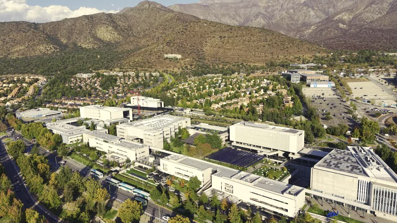 Luftfoto, vidvinkel, der nærmer sig moderne Universidad del Desarrollo campusbygninger beliggende blandt grønne træer med en bjergkulisse. Chile, 4K