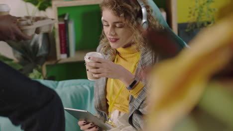 beautiful-young-caucasian-woman-student-using-digital-tablet-computer-colleague-sharing-coffee-with-friends-enjoying-teamwork-connection-in-colorful-office-workplace