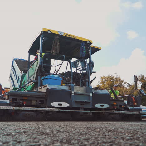 huge asphalt paver machine and workers. fresh asphalt is spreading on the road with new technique and a crew of workers.