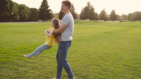 Padre-Feliz-Sosteniendo-A-Su-Pequeña-Hija-Y-Girando-Sobre-Hierba-Verde-En-El-Parque