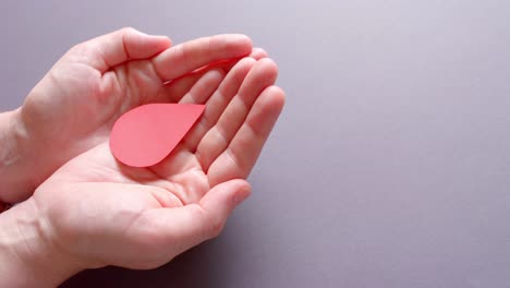 hands of caucasian woman holding blood drop on grey background with copy space, slow motion