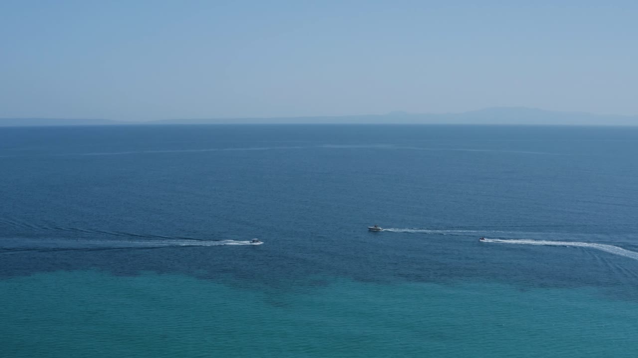 짙은 푸른 바다에서 보트와 제트 스키가 지나가는 공중 슬라이드 왼쪽 샷