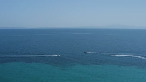 aerial slide left shot of boats and jet ski pass by in dark blue sea