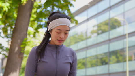 close up of young woman exercising running along city street wearing wireless earbuds stopping to rest 1