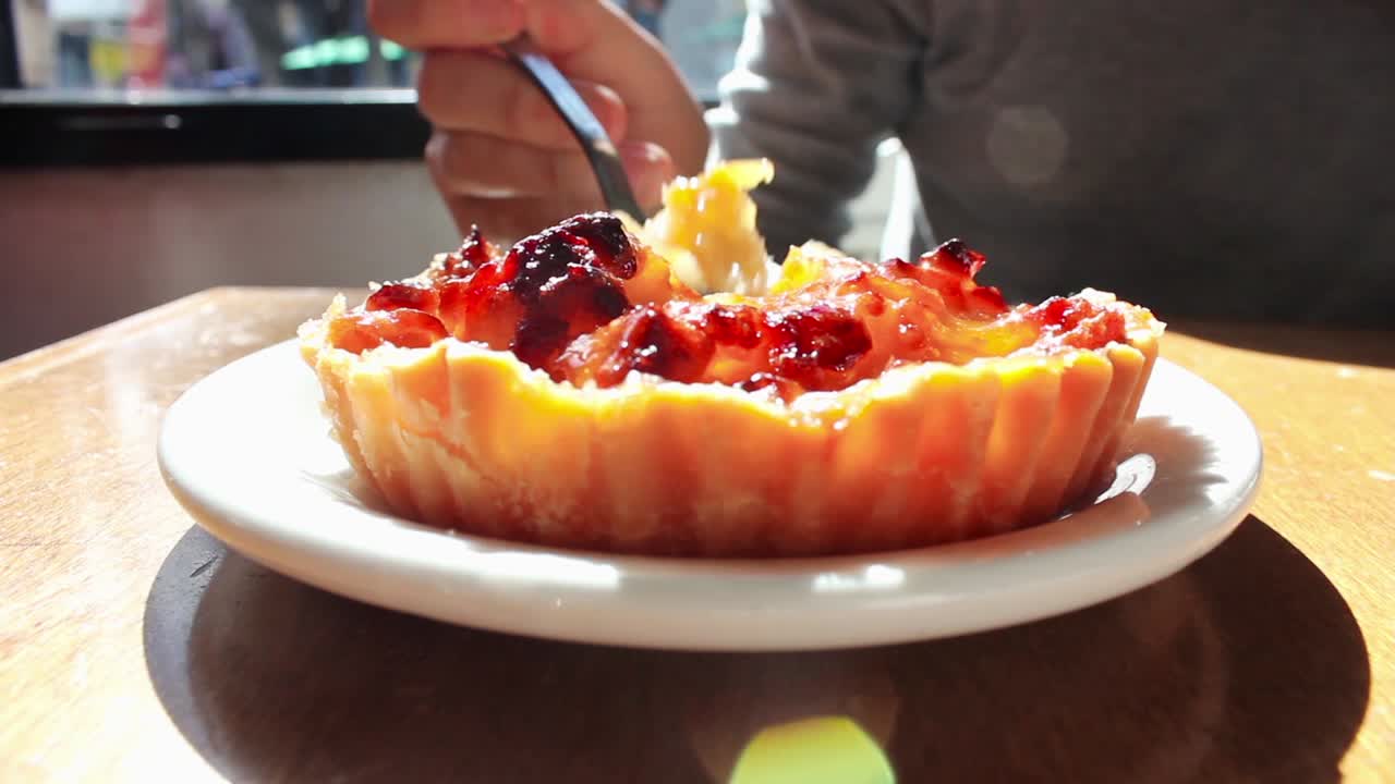 Primo piano di una persona che mangia una deliziosa crostata di frutta con un cucchiaio.