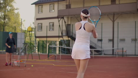 Eine-Tennisspielerin-übt-Das-Schlagen-Des-Balls,-Während-Der-Trainer-In-Zeitlupe-Mit-Einem-Schläger-Auf-Den-Ball-Schlägt.-Training-Einer-Professionellen-Tennisspielerin.