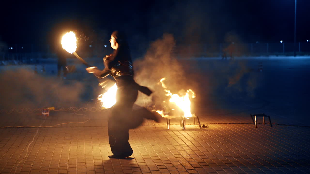 Couple of male dancers move with burning sticks. Fire show performers outdoors at night.