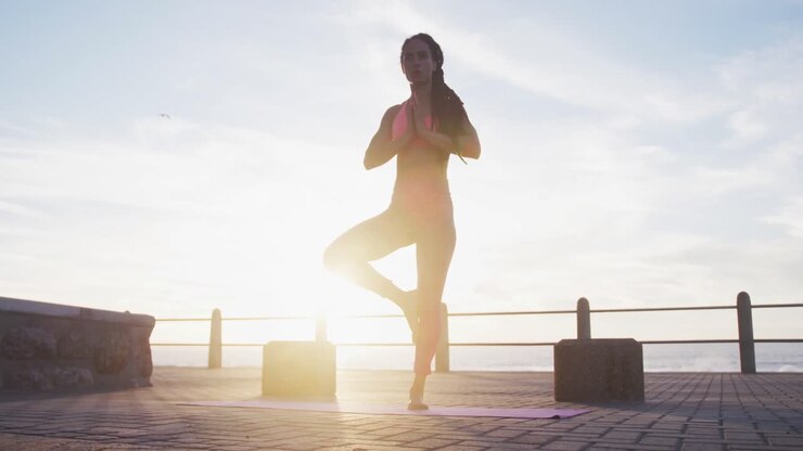 Mujer afroamericana con ropa deportiva haciendo yoga en el paseo marítimo junto al mar.