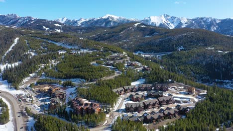 drone glides above big sky, montana in winter, revealing cozy condos, snow-lined roads, and pine forests throughout the mountain town in a peaceful high-elevation alpine setting