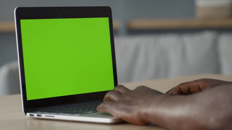 Mains d'homme noir tapant sur un ordinateur portable avec un écran vert (chroma key), travaillant en ligne ou naviguant sur internet.