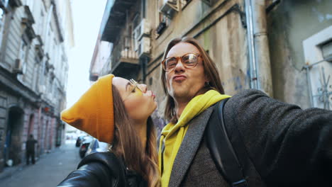 Vista-De-Cerca-De-Una-Pareja-Joven-Y-Guapa-Sonriendo-Y-Posando-Para-La-Cámara-Mientras-Se-Toma-Selfie-En-La-Calle