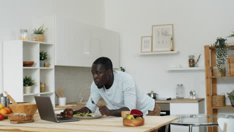 Hombre-Afroamericano-Usando-Laptop-Y-Comiendo-Ensalada-En-Casa