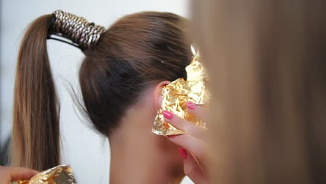 Makeup-artist-applying-golden-pieces-of-metallic-paper-on-the-model's-face.-Golden-skin-make-up.-Close-Up-view