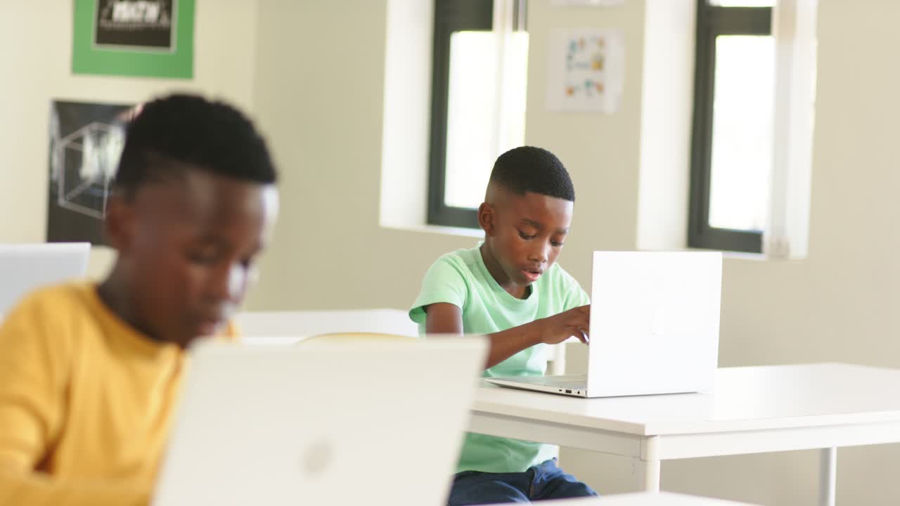 Ragazzi afroamericani in classe che digitano su portatili bianchi, cambiando attenzione, che spronano un ragazzo vestito di verde ad alzare la mano