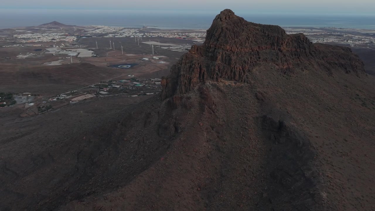Maestosa prospettiva aerea del monumento naturale Roque Aguayro, una formazione vulcanica in un paesaggio arido con una città costiera in lontananza