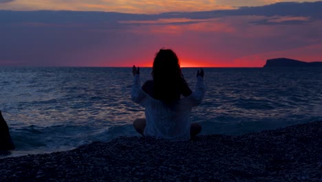 silhouette of woman concentrated on yoga pose exercising on the beach during colorful sunset