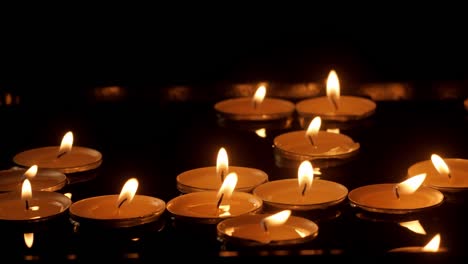 close up burning candles floating on water surface in dark. scented aroma candles float in dark water while relaxing spa therapy.