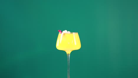 a vibrant yellow cocktail with garnish against a green screen backdrop, highlighting its vivid color and elegant presentation