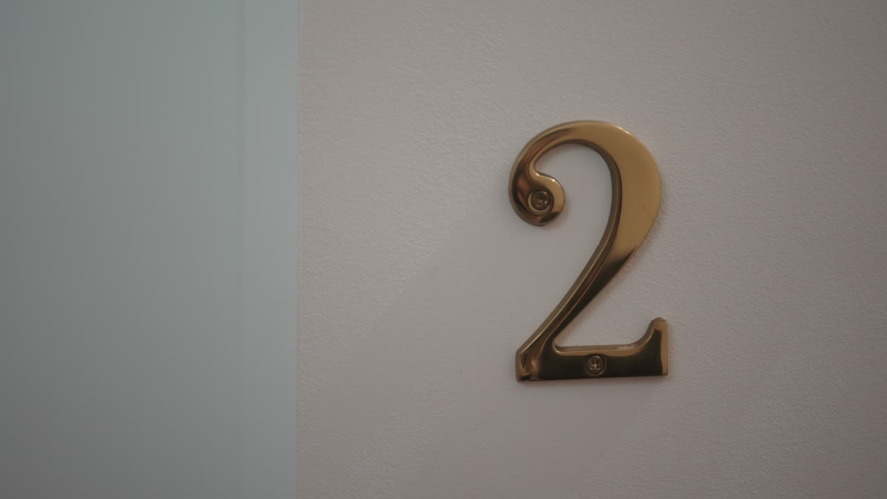 Shiny golden number two fixed on a white door surface in a minimalist interior setting
