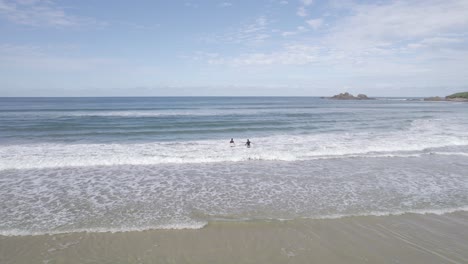 Tourists-Walking-Into-The-Sea-Opposing-Foamy-Waves-In-Byron-Bay,-New-South-Wales,-Australia