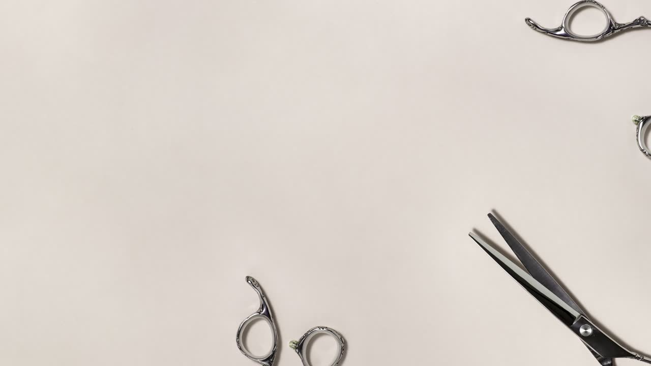 Flat lay of professional silver hair cutting shears set frame moves to the left on beige background. Hairdresser salon equipment and haircut work tools concept during quarantine with copy space