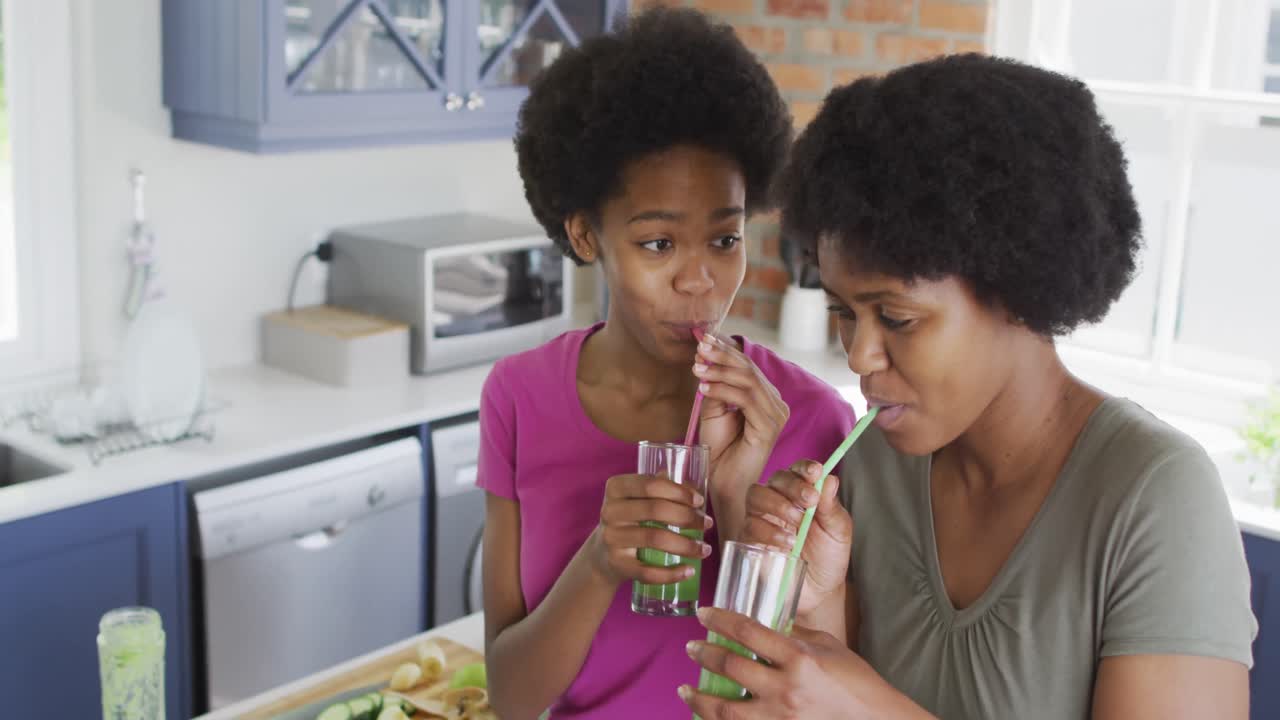 Heureuses mère et fille afro-américaines buvant une boisson saine dans la cuisine