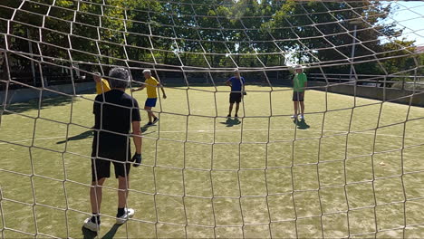 back view of a senior goalkeeper standing in football goal training with friends and catching ball