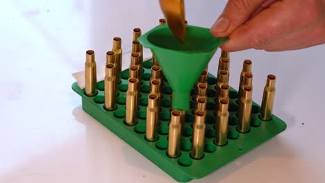 person filling empty brass casing with gunpowder through funnel during home reloading process - static closeup of hand and tray with caliber 3006 empty brass casings