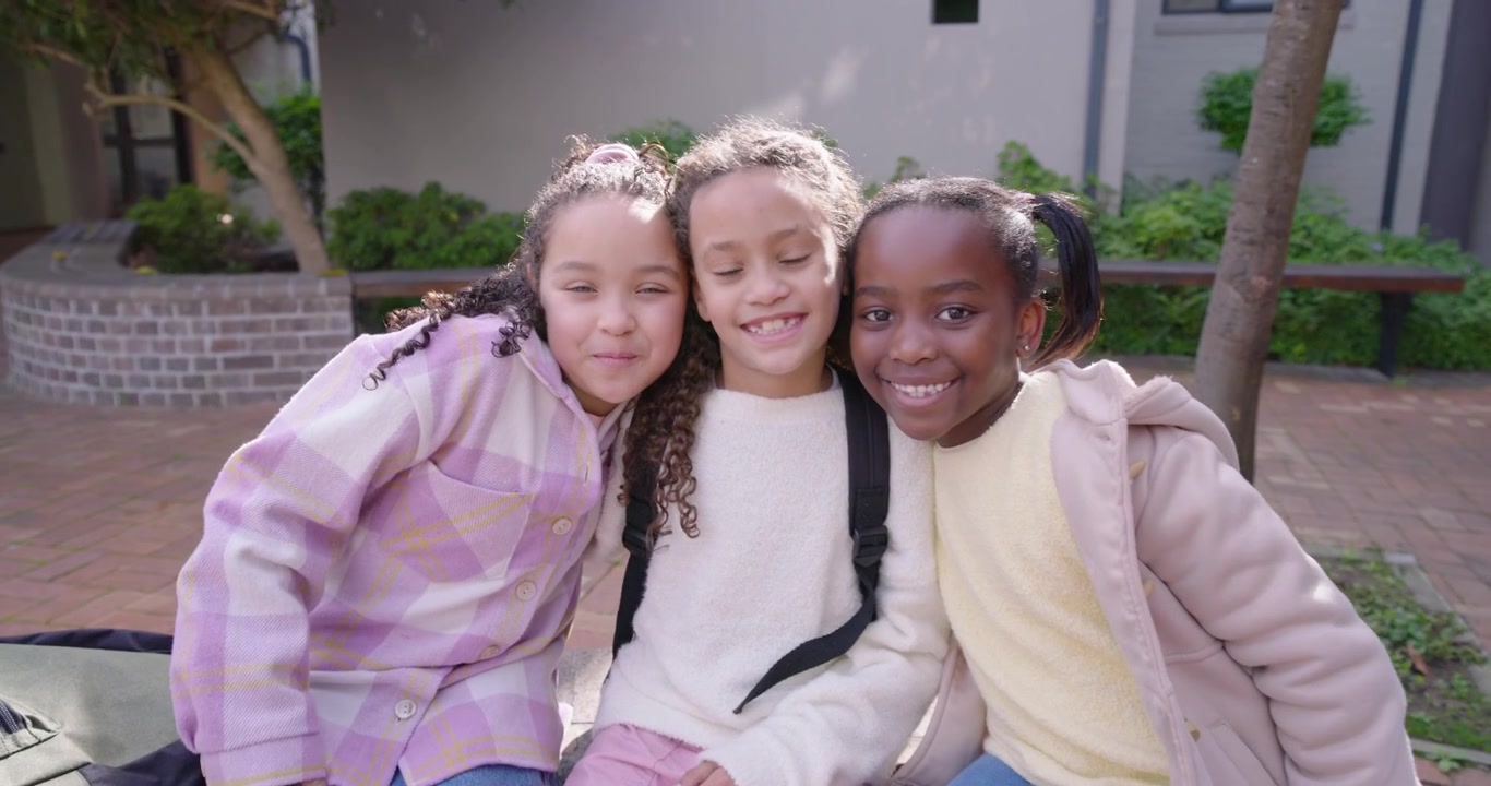 African-American schoolgirls sitting school bench backpack left girl talking leaning hugging posing