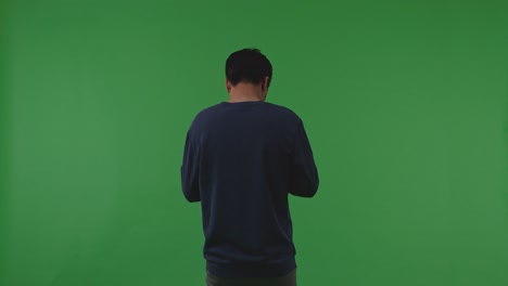 우울한 아시아 난민 남성의 뒷면은 녹색 스크린 배경에 서있는 동안 전쟁에서 절망에 검은 머리카락을 통해 손을 문지르고 있습니다.