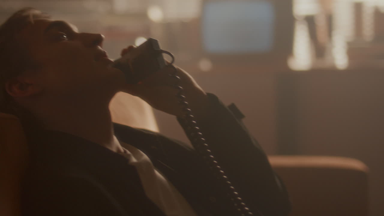 Giovane uomo appoggiato al divano, parla al telefono retrò con filo