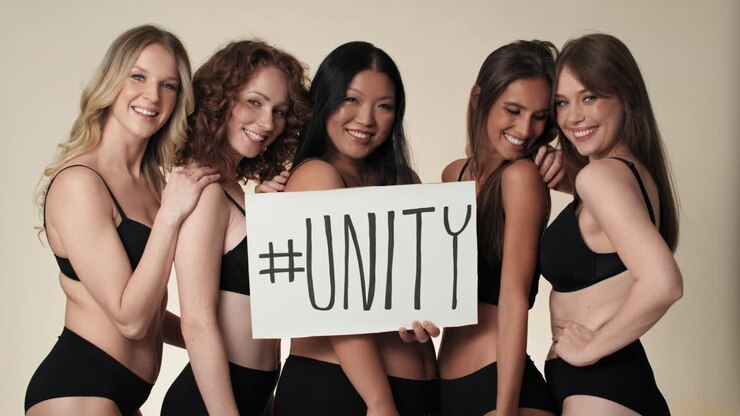 Ritratto di gruppo di donne in intimo, in piedi nello studio e che tengono uno striscione.